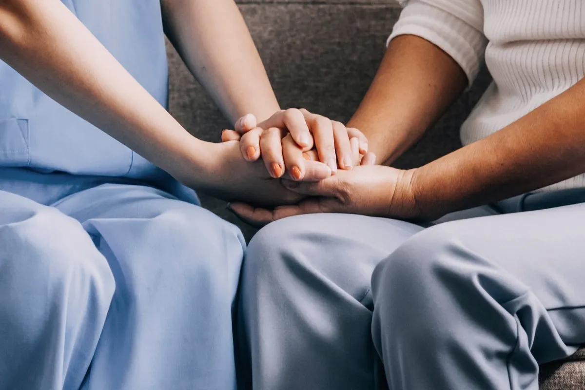 A carer in blue scrubs holding a client's hands